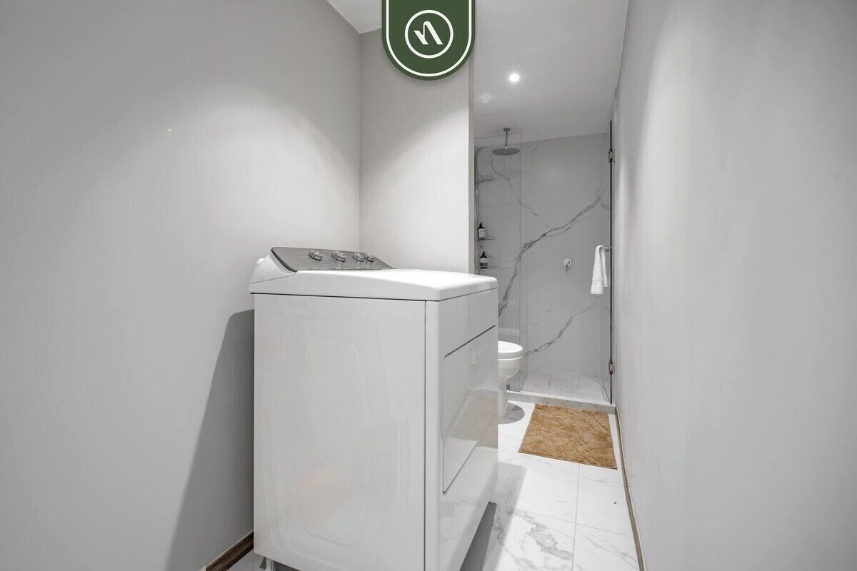 Un baño moderno y funcional con lavadora y secadora integradas, ducha de mármol y váter.