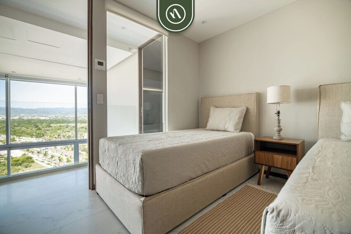 A bedroom with a large bed, a nightstand, a lamp, and a view of the outdoors.