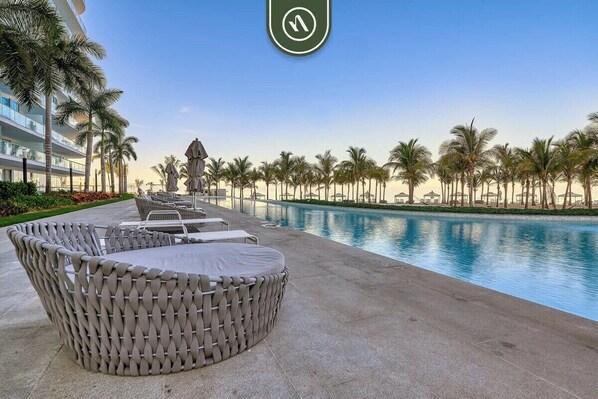 A poolside area with wicker furniture and a view of the pool and palm trees. - Stunning Oceanview Two Story Condo - Beach - Gym (Nuevo Nayarit)