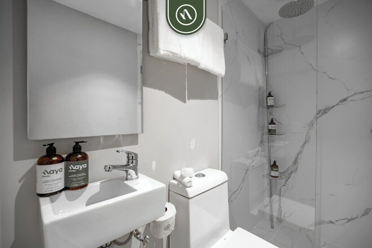 A modern bathroom with a white sink, a mirror, and a marble shower wall.