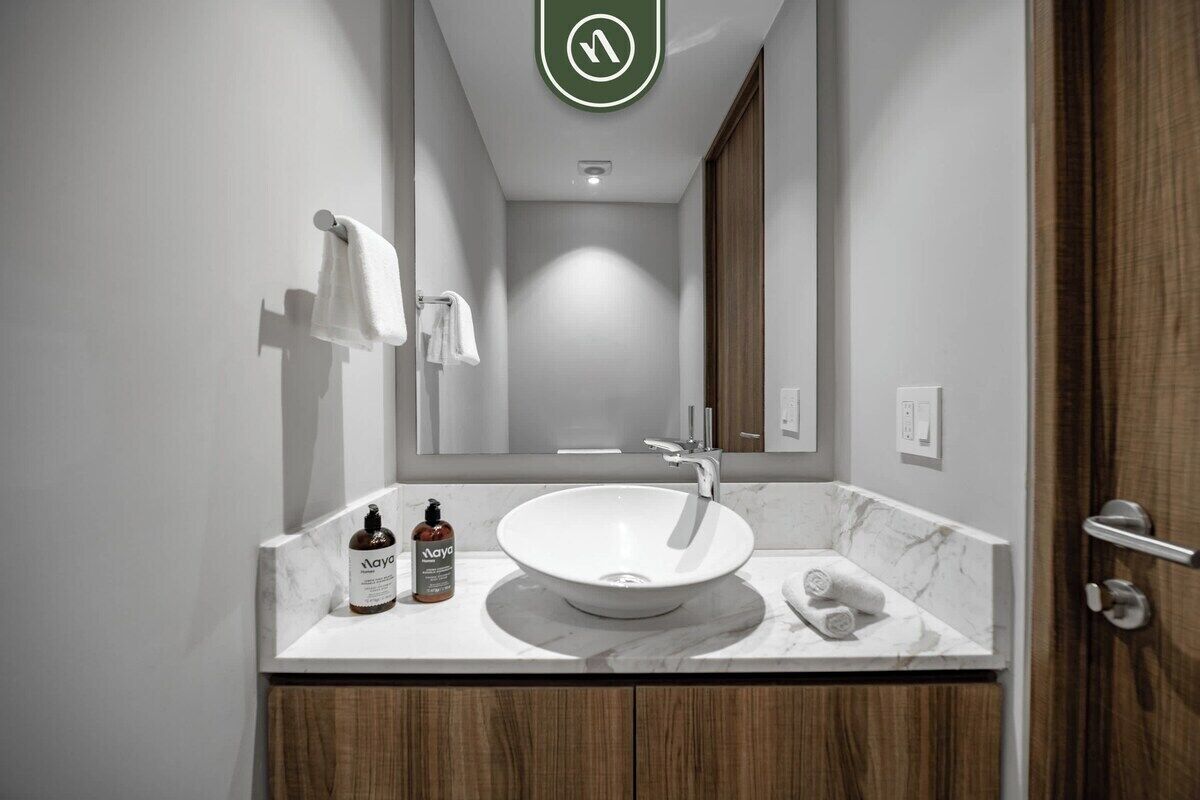 Un baño moderno con un lavamanos blanco, un espejo y un perchero para toallas.