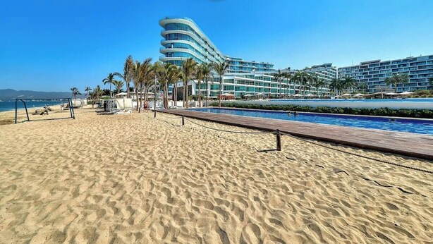 A beach with a wooden boardwalk, palm trees, and a modern hotel with multiple balconies. - Oceanview 1 BR Condo - Private Beach - Pools (Nuevo Nayarit)