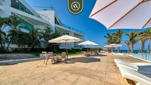 A modern outdoor patio with seating and umbrellas, overlooking a pool and beach. - Oceanview 1 BR Condo - Private Beach - Pools (Nuevo Nayarit)