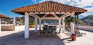 Un espace extérieur aménagé, abrité et doté d’un toit en tuiles, avec une table, des chaises et des plantes en pot.