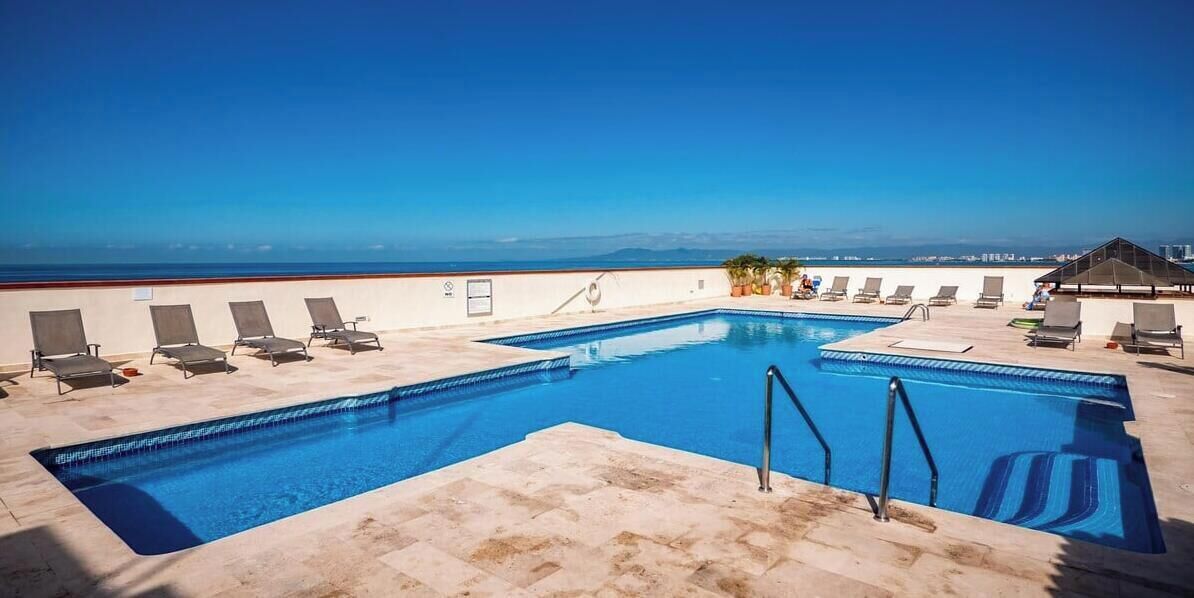 Une piscine sur le toit, avec une eau d’un bleu cristallin, entourée de chaises longues et offrant une vue sur l’océan.