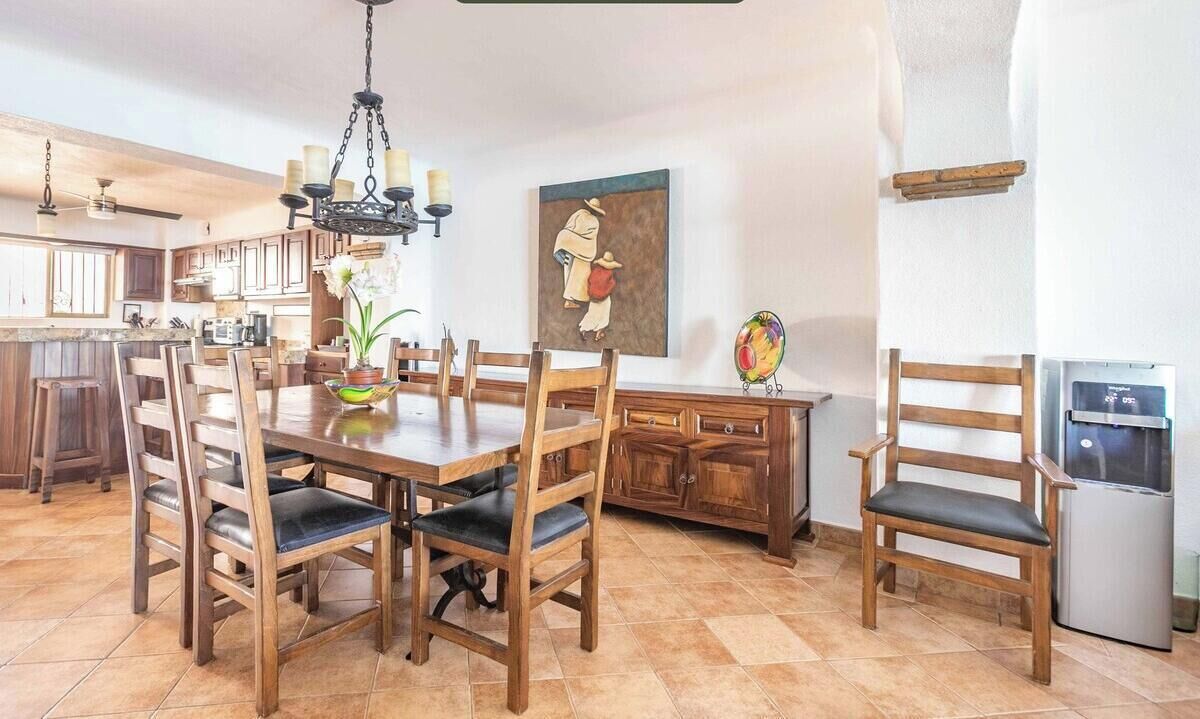 A spacious kitchen with wooden cabinets, a dining table with chairs, a chandelier, and a refrigerator.