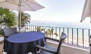 A balcony with a table and chairs, a view of the sea, and a palm tree.