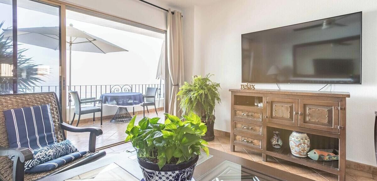 A living room with a TV, a potted plant, a dining table, and a balcony with a view.