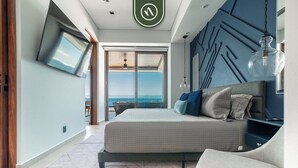 Ein modernes Schlafzimmer mit Bett, Fernseher und Meerblick.