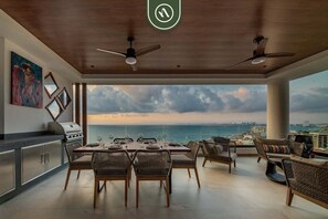 A modern kitchen with a view of the ocean, dining area with wicker furniture, and ceiling fans. - Luxury 2 BR Condo With Beachview - Rooftop Pool (Puerto Vallarta)