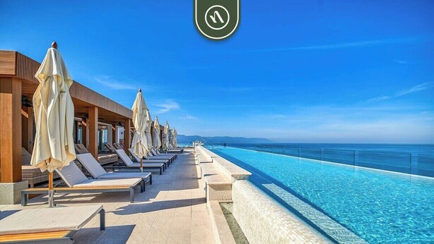Ein Poolbereich mit Liegestühlen und Sonnenschirmen, bewölkter Himmel und Blick auf den Ozean.