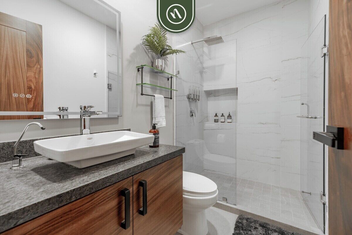 A modern bathroom with a large sink, wooden cabinets, a toilet, and a glass shower enclosure.