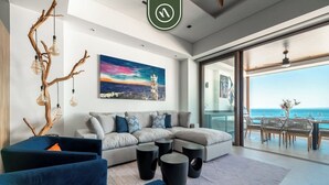Ein modernes Wohnzimmer mit einer Eckcouch, einem blauen Sessel und einem Couchtisch. An der Wand hängt ein Gemälde von einem Leuchtturm, und große Fenster bieten Blick auf den Ozean.
