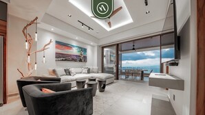 Ein modernes Wohnzimmer mit einer Eckcouch, einem dunklen Sessel, einem Essbereich und einem großen Fenster mit Blick auf die Stadt.