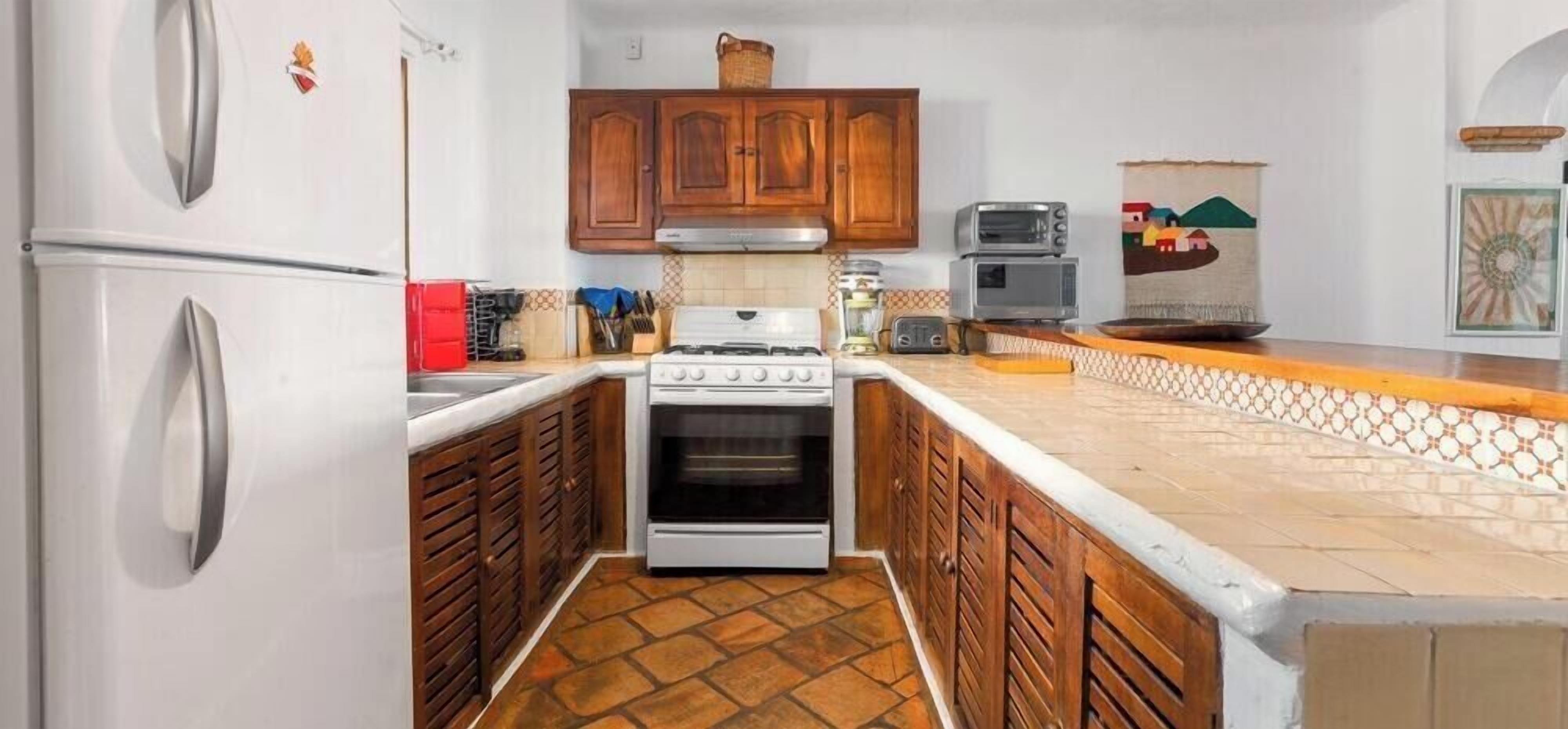 Cocina compacta con estufa, horno y dos hornos integrados. Cuenta con gabinetes de madera y una salpicadera de azulejos.