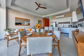 A modern dining area with a round table, grey upholstered chairs, and a ceiling fan.