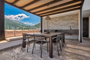 A modern outdoor dining area with a stone floor, a wooden table, and chairs.