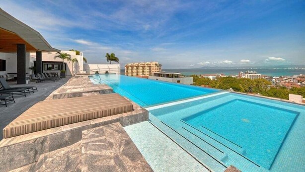A swimming pool with a view of the ocean and cityscape, lounge chairs, and a covered seating area. - Amazing 2BR Apt -private Balcony - Rooftop Pool (Puerto Vallarta)