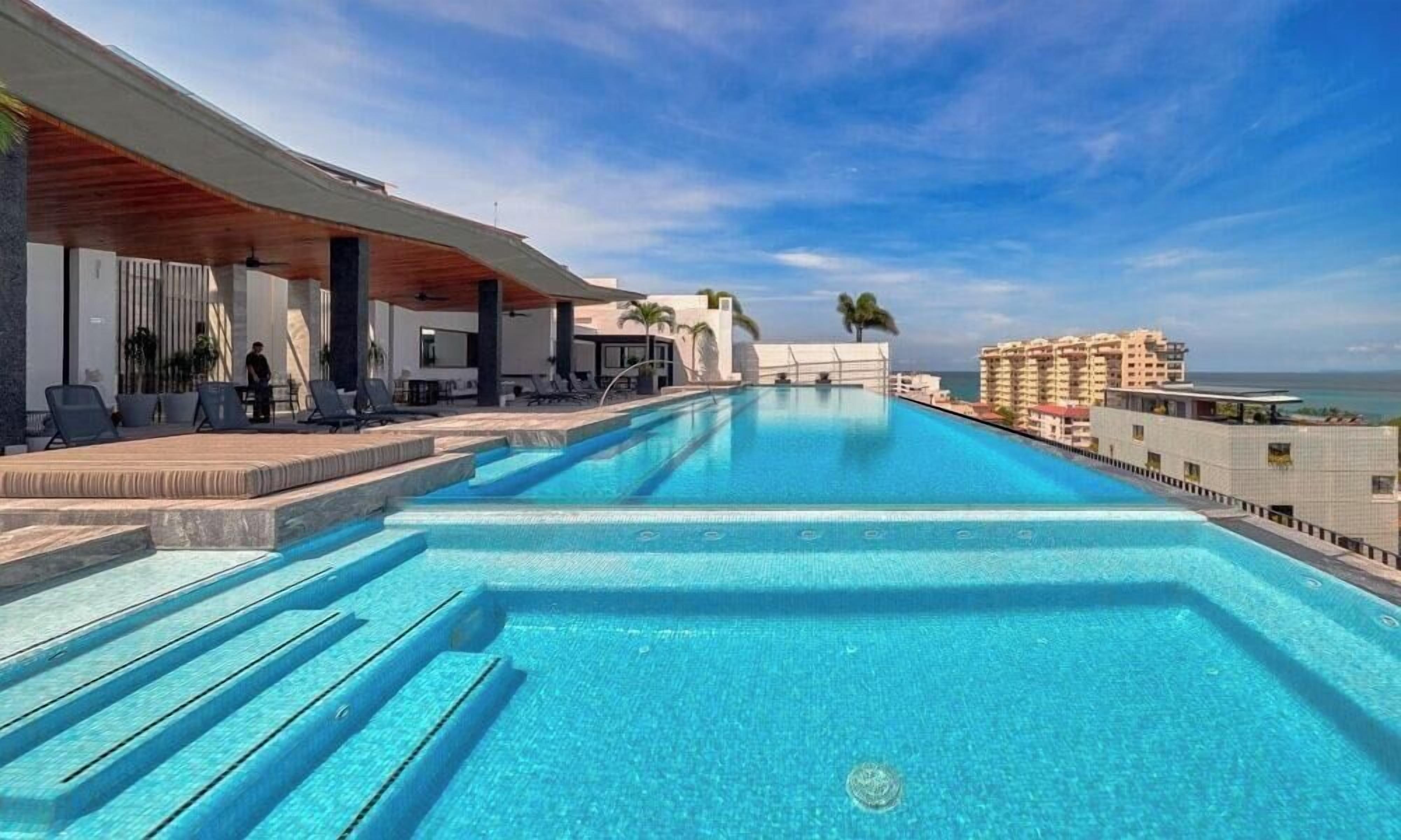 A swimming pool with steps leading into it, surrounded by lounge chairs and a building with a modern design.