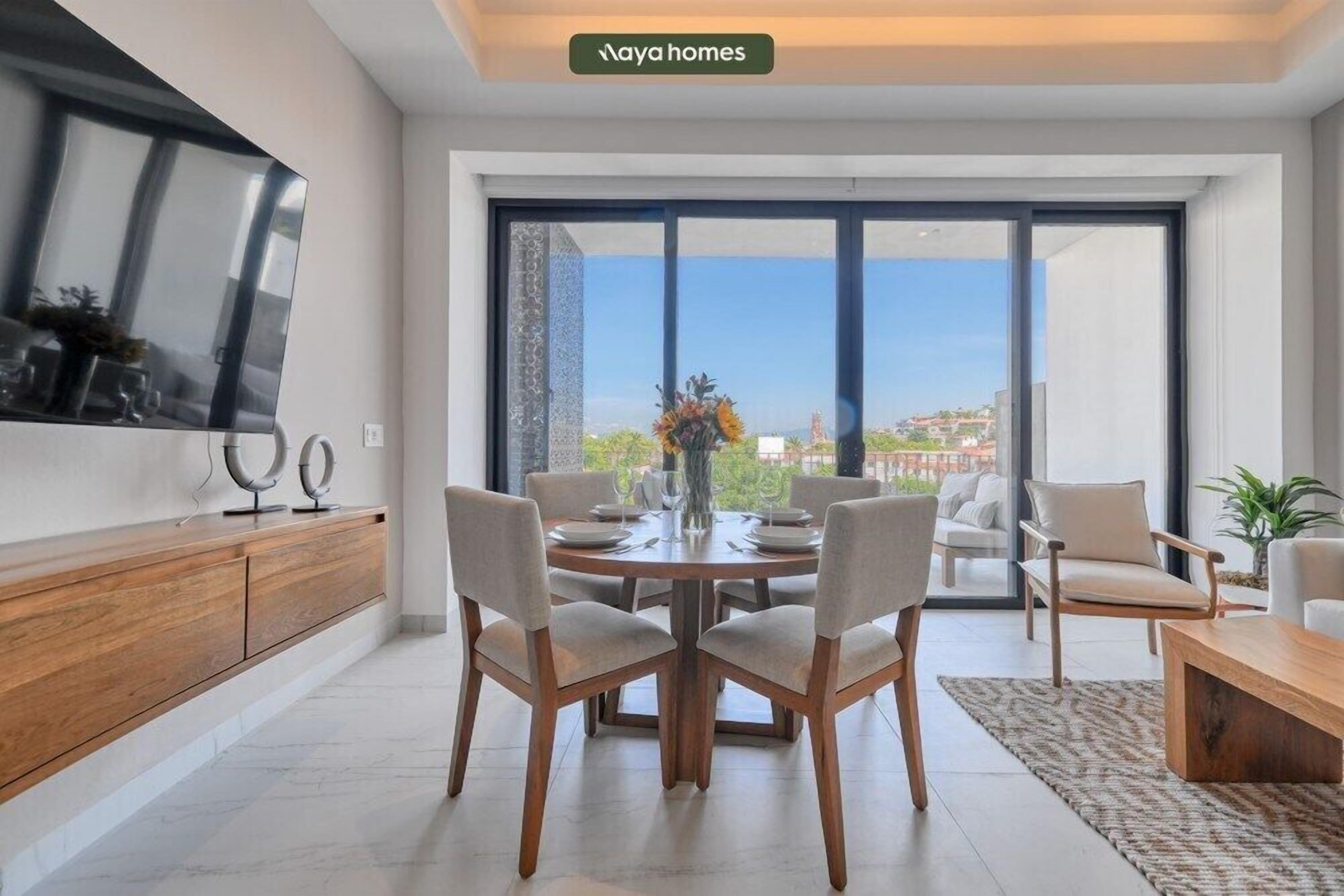 A modern living room with a dining table, chairs, a TV, and a large window with a city view.