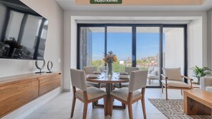 A modern living room with a dining table, chairs, a TV, and a large window with a city view. - Amazing 2BR Apt -private Balcony - Rooftop Pool (Puerto Vallarta)