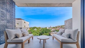 A balcony with two sofas and a table, a patterned wall, and a view of buildings and greenery. - Amazing 2BR Apt -private Balcony - Rooftop Pool (Puerto Vallarta)