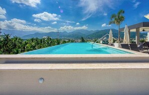 A swimming pool with a view of mountains, surrounded by palm trees and lounge chairs. - Amazing 2 BR Condo in Versalles - Rooftop Pool (Puerto Vallarta)