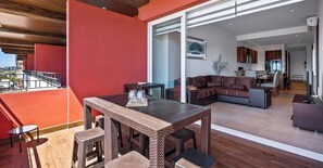 Un vaste espace de vie comprenant une table et des chaises en bois, un ensemble de canapés et une vue sur la ville grâce à de grandes fenêtres.