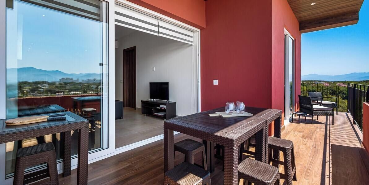 Ein Balkon mit Holzboden, einem Tisch mit Stühlen und einem Fernseher im Hintergrund.