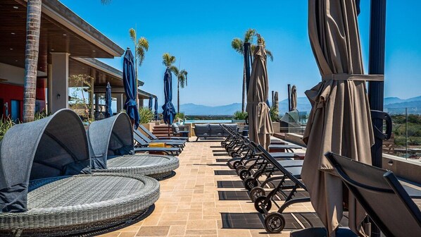 A rooftop lounge with wicker chairs, umbrellas, and a view of the mountains.