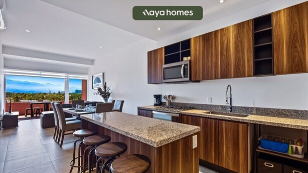 A modern kitchen with wooden cabinets, a granite countertop, and a large island with bar stools. - Equipped 3BR House - Pool - Gym - 5 min to Beach (Nuevo Nayarit)