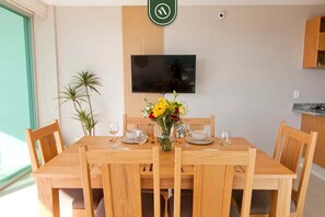 Ein Essbereich mit Holztisch, Stühlen, einer Blumenvase, einem wandmontierten Flachbildfernseher und einem Topfpflanzen.