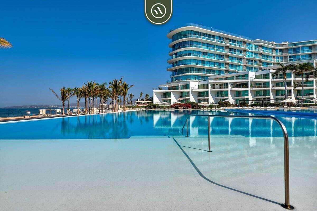 Un hotel moderno con una piscina grande, palmeras y una vista despejada del océano.