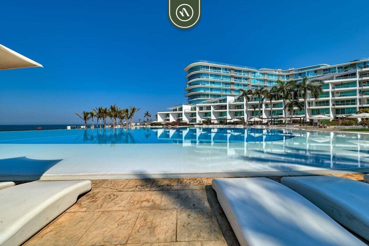 A hotel with a large pool, palm trees, and a clear blue sky.