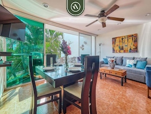 Uma área de refeições com mesa de vidro, cadeiras e vista para o verde lá fora.