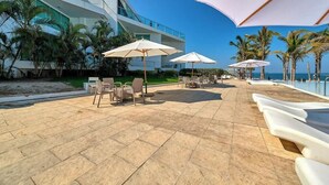 Une terrasse d’hôtel avec des espaces de détente en plein air, des palmiers et une vue sur la piscine.