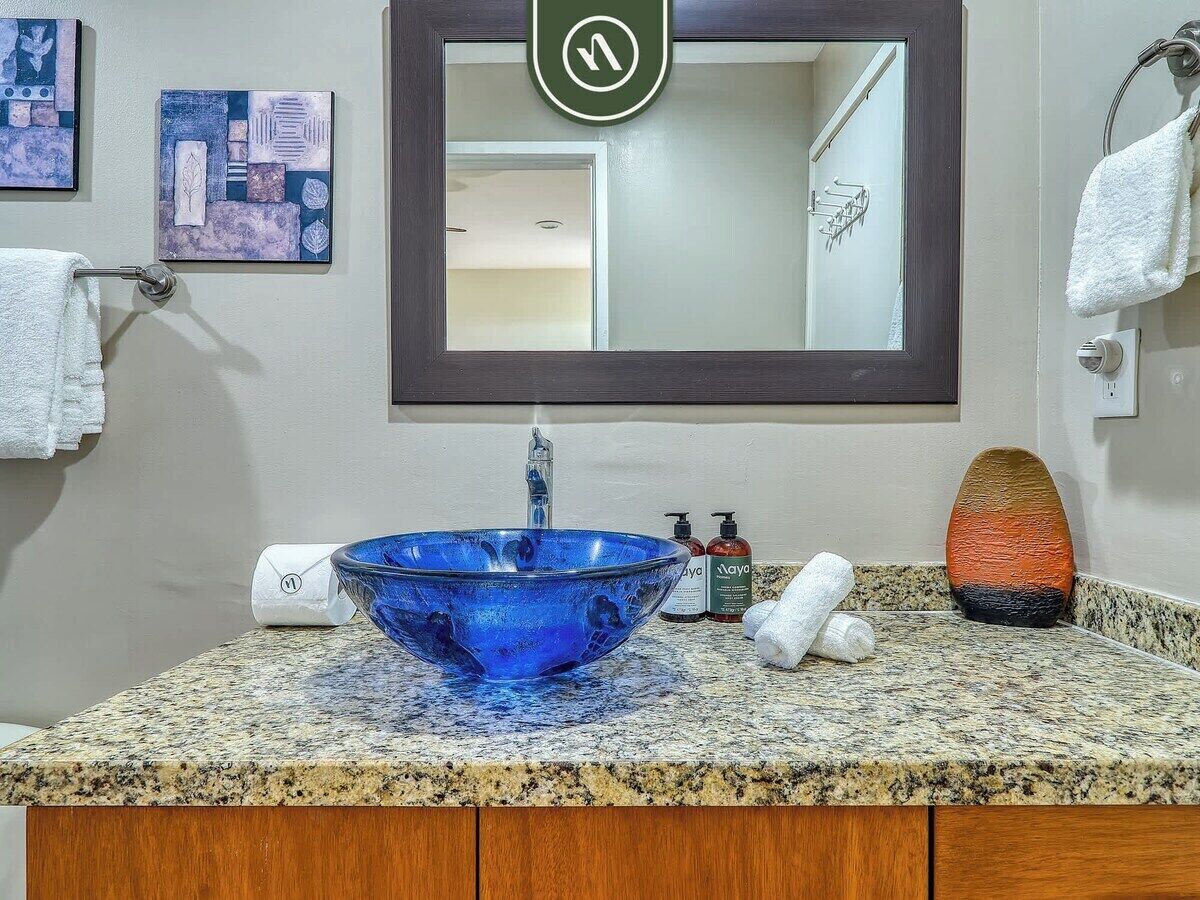 A bathroom with a blue glass sink, a mirror, a towel rack, and a granite countertop.