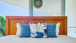 Un lit avec une tête de lit en bois, trois oreillers et une vue sur l’extérieur.