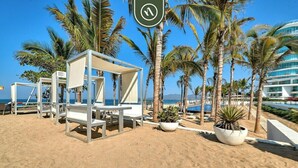 Un hôtel situé en bord de mer, doté de chaises longues blanches, de palmiers et offrant une vue dégagée sur l’océan.