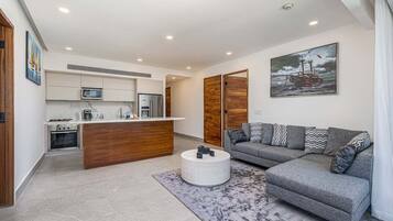 A modern living room with a grey sofa, a round coffee table, and a kitchen area with a microwave and refrigerator.