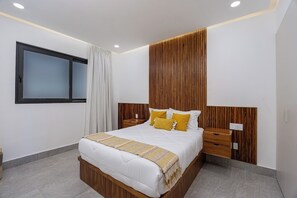 Quarto de hotel moderno com uma cama grande, cabeceira de madeira, mesas de cabeceira e uma janela com cortinas.