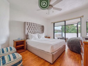 A bedroom with a large bed, wooden flooring, a ceiling fan, a window with a view, and a small table with a bowl. - 2 BR Condo in Hotel - Beach - Pools - Kids Club (Puerto Vallarta)