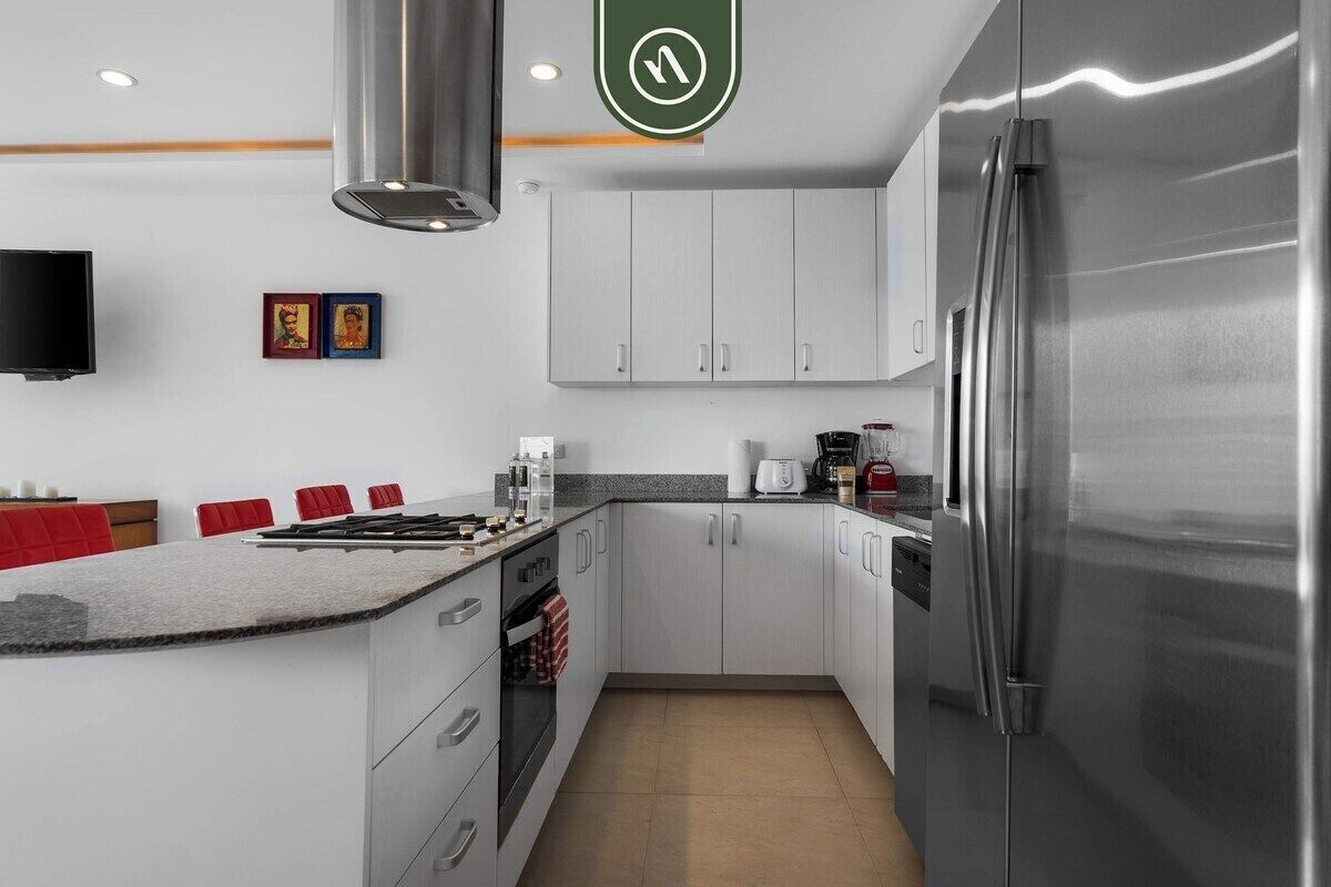A modern kitchen with stainless steel appliances, a granite countertop, and a flat-screen TV.