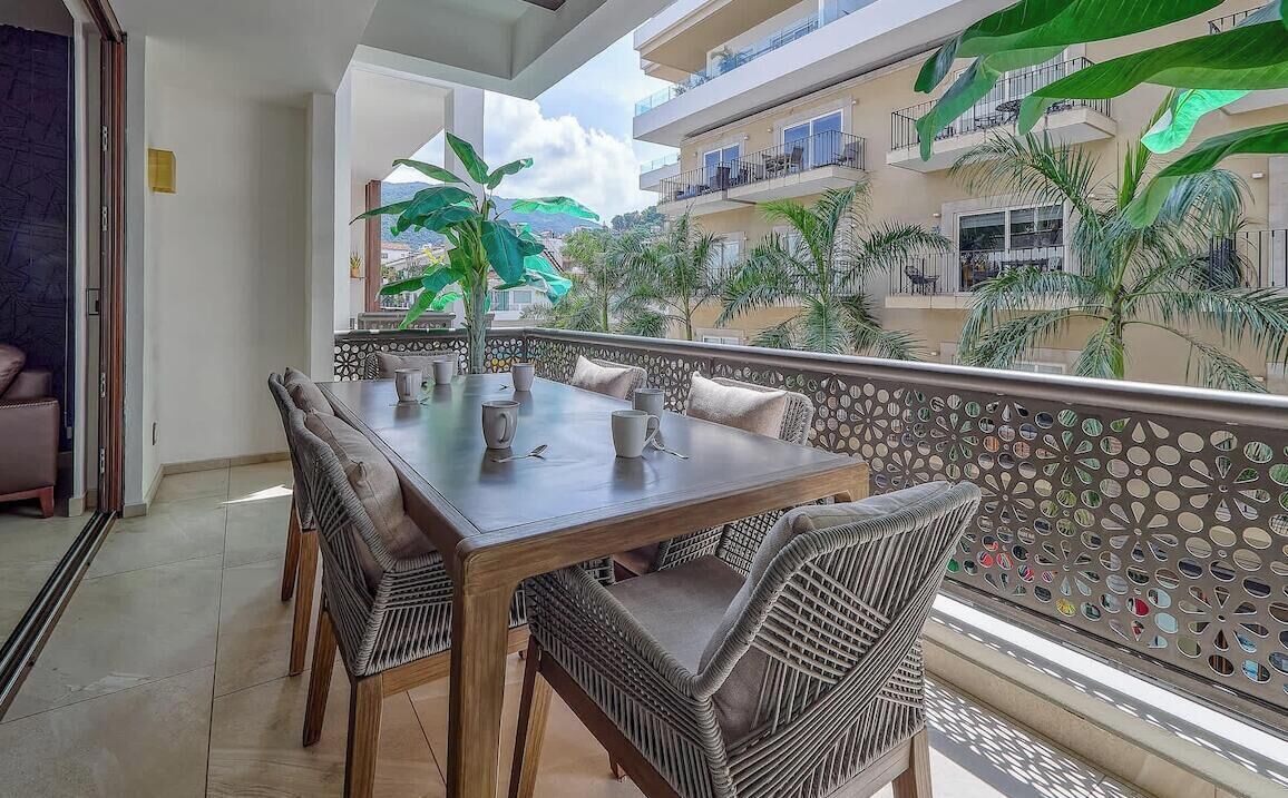 A balcony with a dining table, chairs, and a view of a building with balconies and palm trees.
