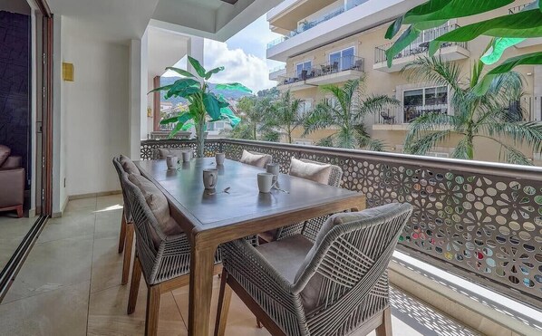 Een balkon met een eettafel, stoelen en uitzicht op een gebouw met balkons en palmbomen.