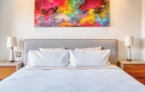A bed with a quilted white cover, a grey headboard, and two bedside lamps. - Luxury 2BR Condo in Romatic Zone - Rooftop Pool (Puerto Vallarta)