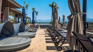 A rooftop terrace with wicker lounge chairs, umbrellas, and a view of mountains. - Luxury 2BR Condo in Nuevo Vallarta - Rooftop Pool (Nuevo Nayarit)