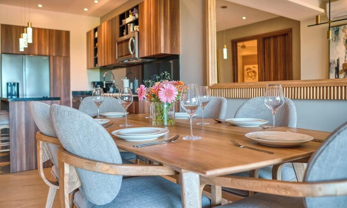 A dining area with a wooden table set for six, surrounded by grey upholstered chairs.