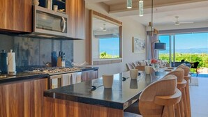 A modern kitchen with a central island, wooden cabinets, and a large window offering a view of the outdoors. - Luxury 2BR Condo in Nuevo Vallarta - Rooftop Pool (Nuevo Nayarit)