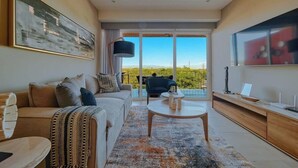 A modern living room with a sofa, coffee table, and a view of the outdoors. - Luxury 2BR Condo in Nuevo Vallarta - Rooftop Pool (Nuevo Nayarit)